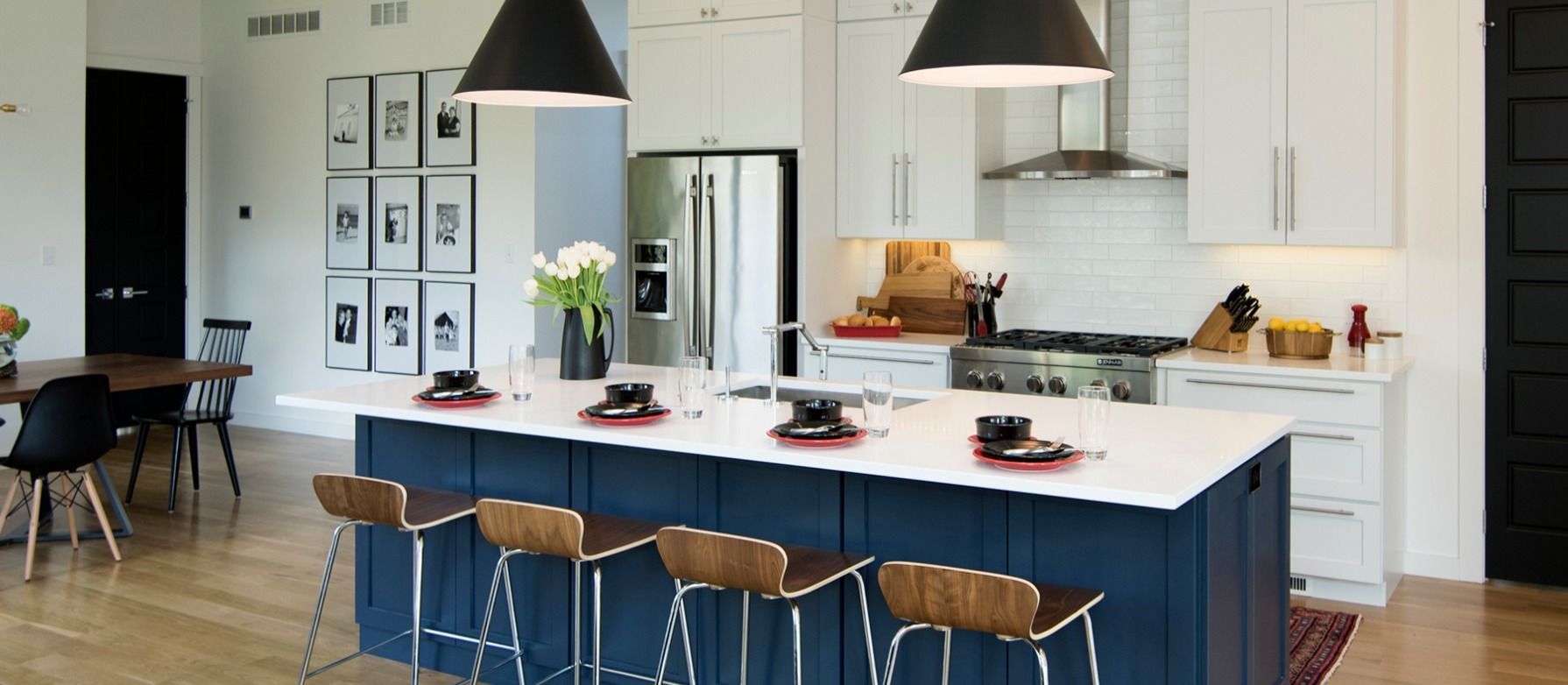 Modern kitchen with blue island, white countertops, and black pendant lights.