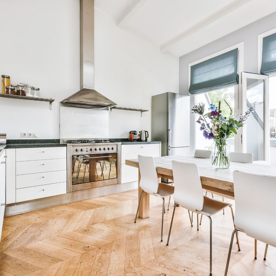 Modern kitchen with white cabinets, stainless steel appliances, and a wooden table with white chairs.