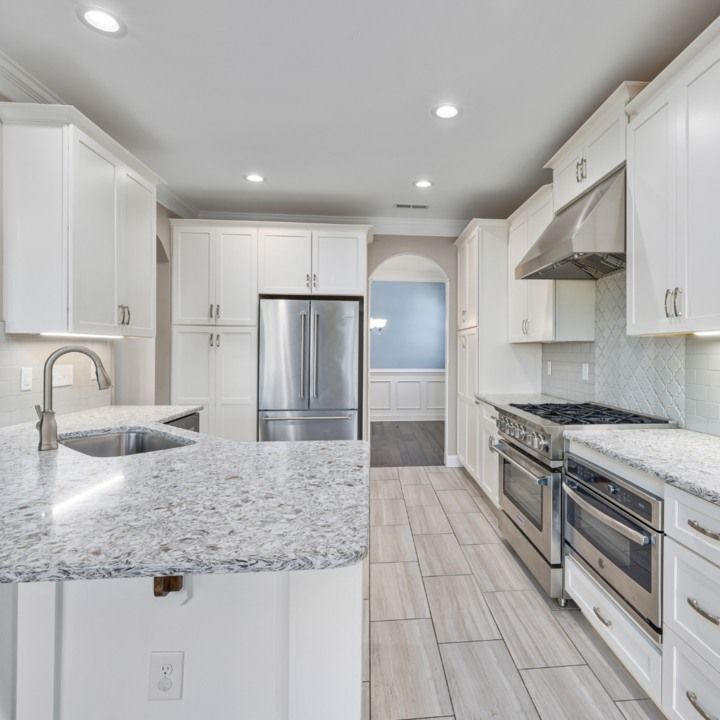 White kitchen with stainless steel appliances, granite countertops, and light gray tile flooring.