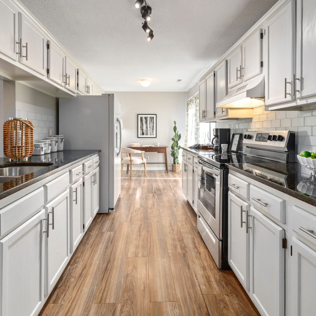 Bright, galley kitchen with white cabinets, stainless steel appliances, and wood-look flooring.