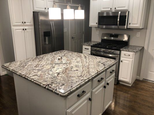 White kitchen with granite island and stainless steel appliances.