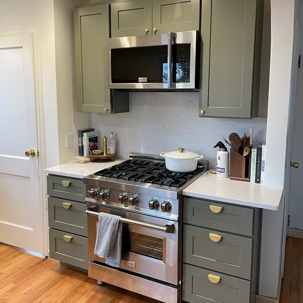 Green kitchen cabinets surround a stainless steel range with white countertops and microwave.