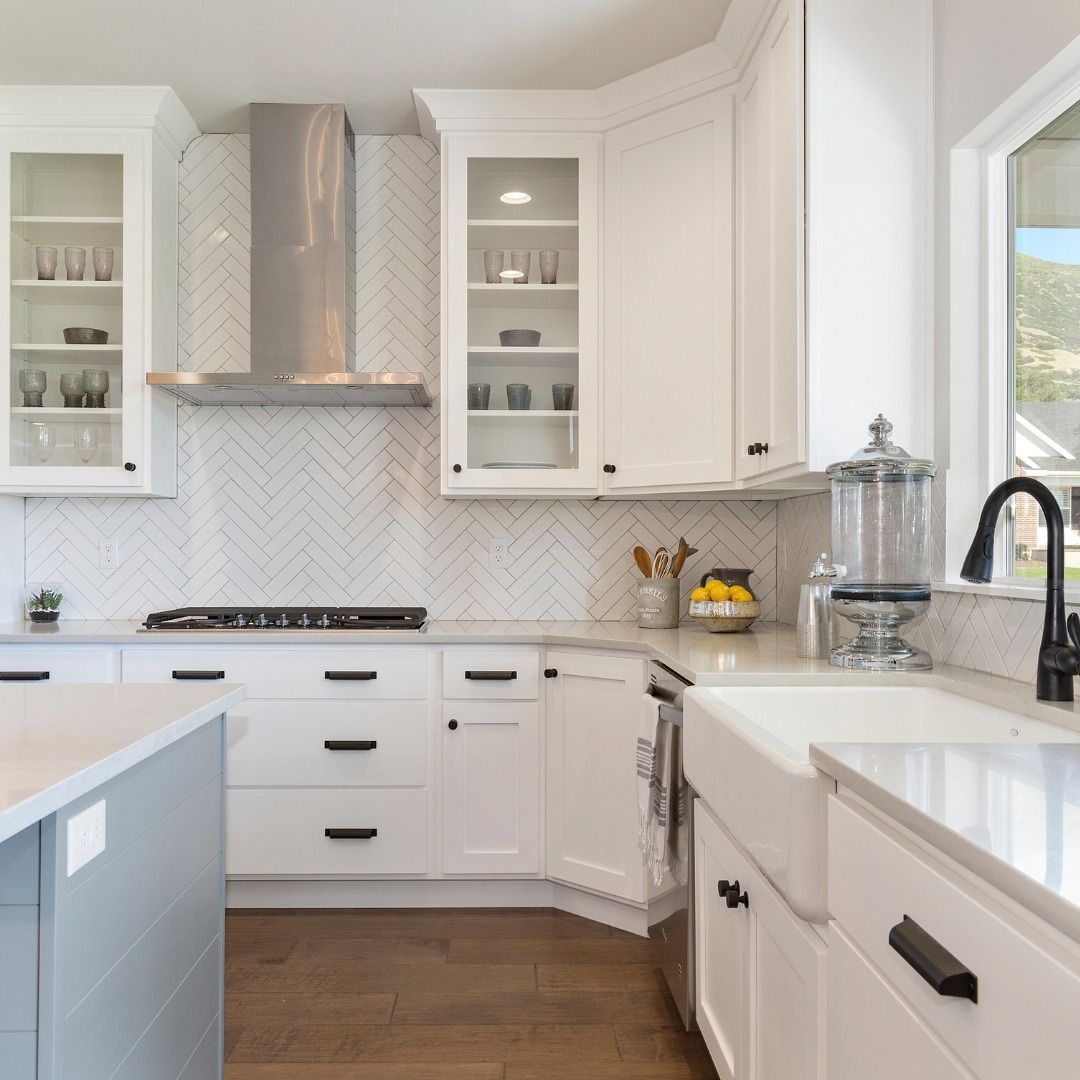 White kitchen with herringbone backsplash, stainless steel hood, and black hardware.
