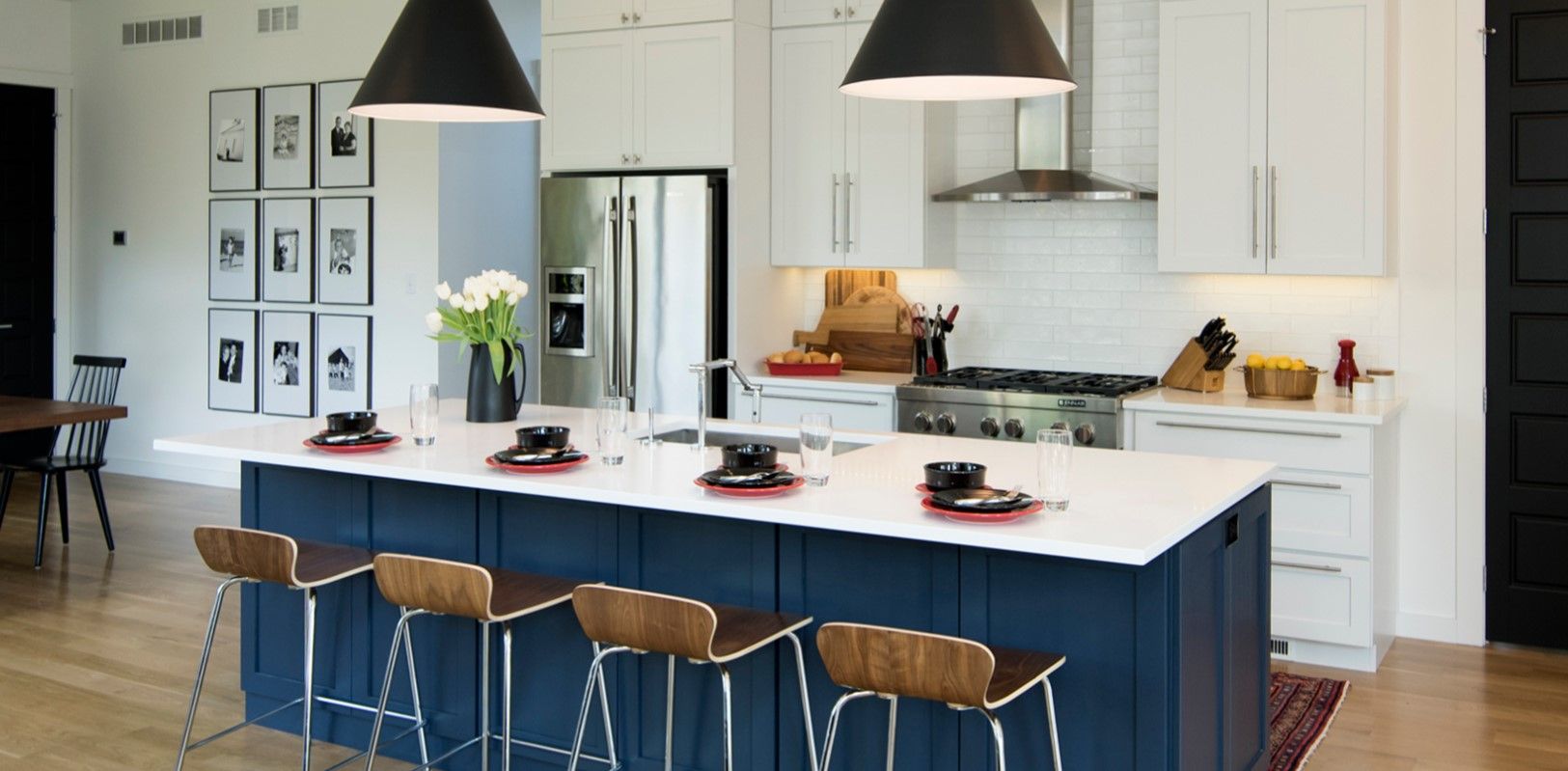 Modern kitchen with blue island, white countertops, black pendant lights, and wooden stools.