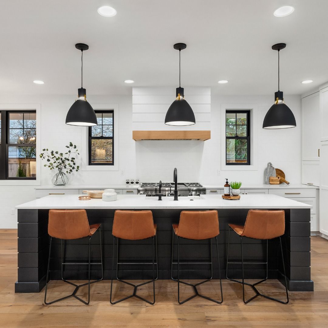 Modern kitchen island with black base, white countertop, brown bar stools, and pendant lights.