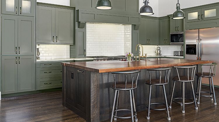 Green kitchen with wooden island, stainless steel appliances, and dark wood floors.