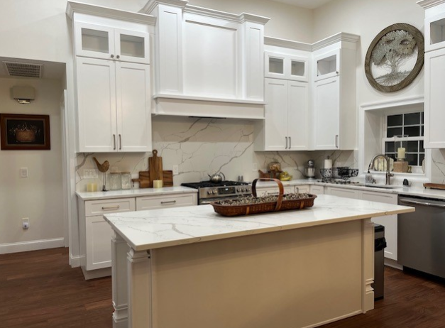 White kitchen with island and marble countertop, stainless steel appliances, and wood floors.