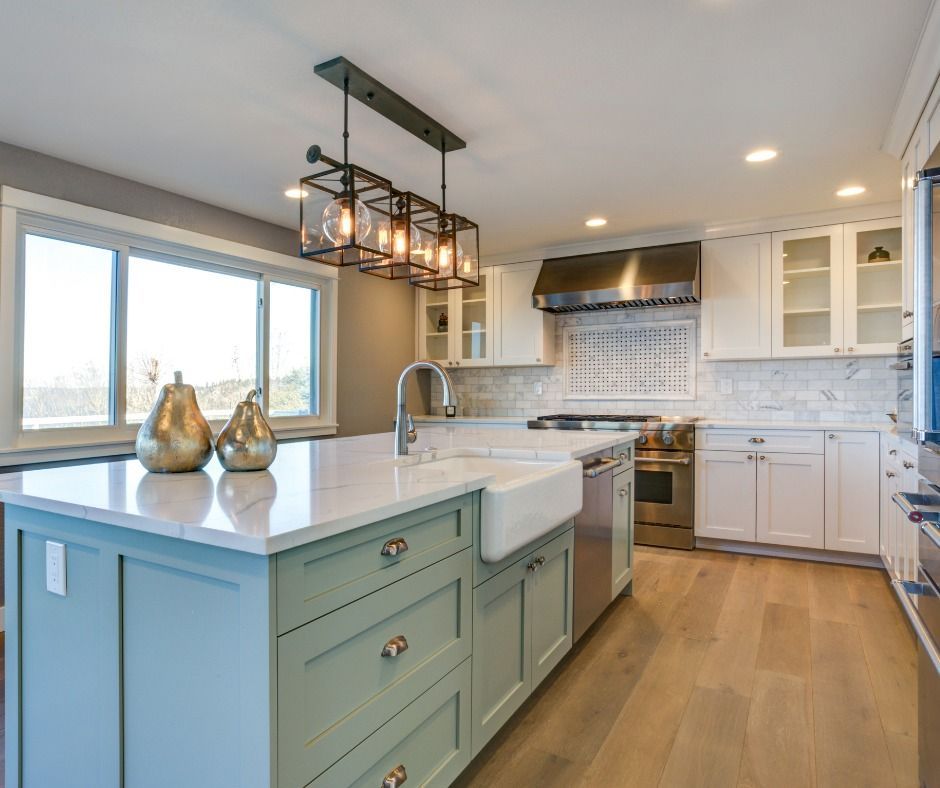 Modern kitchen with blue-green island, white countertops, stainless steel appliances, and wood floors.