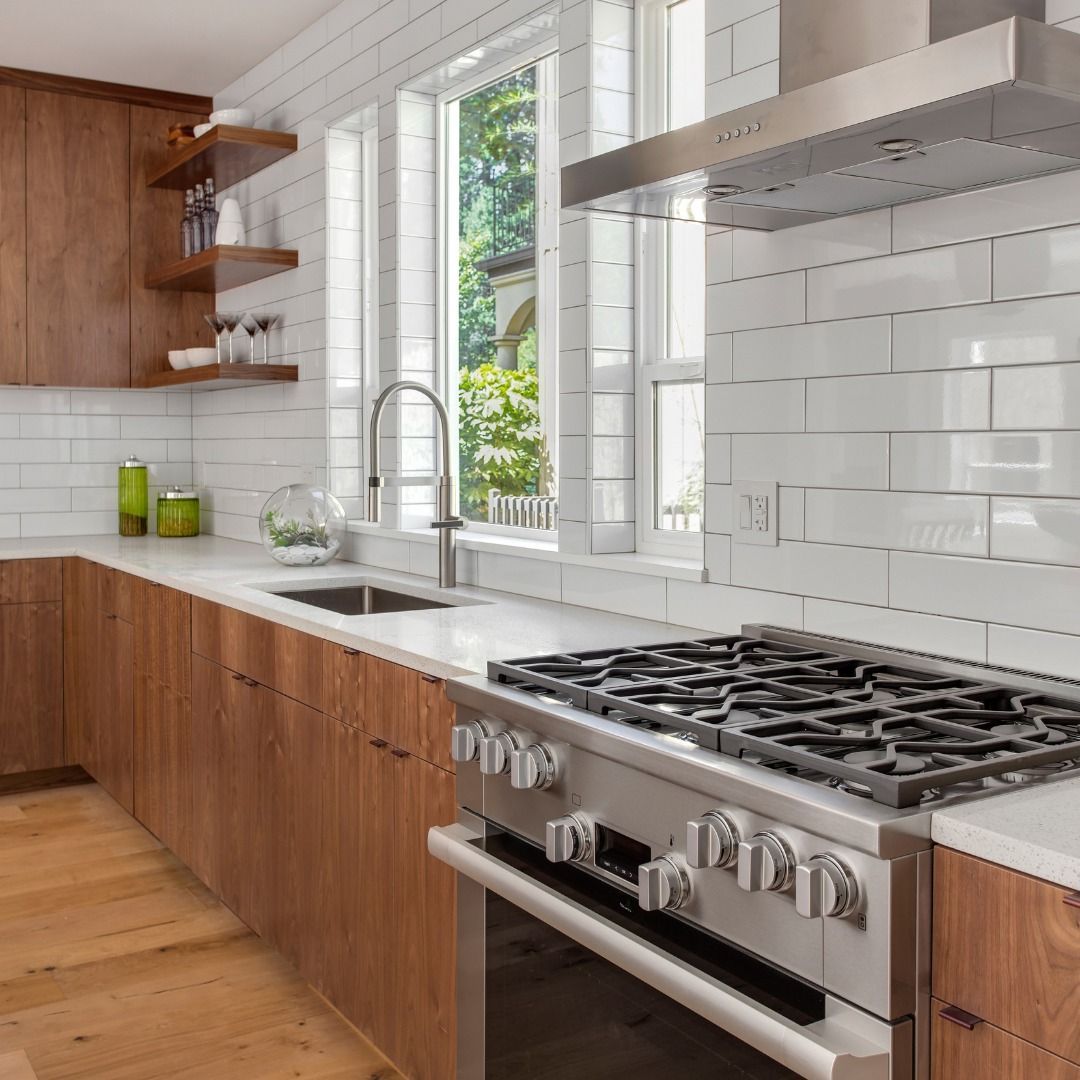 Modern kitchen with wood cabinets, white countertops, subway tile, stainless steel appliances, and a window.