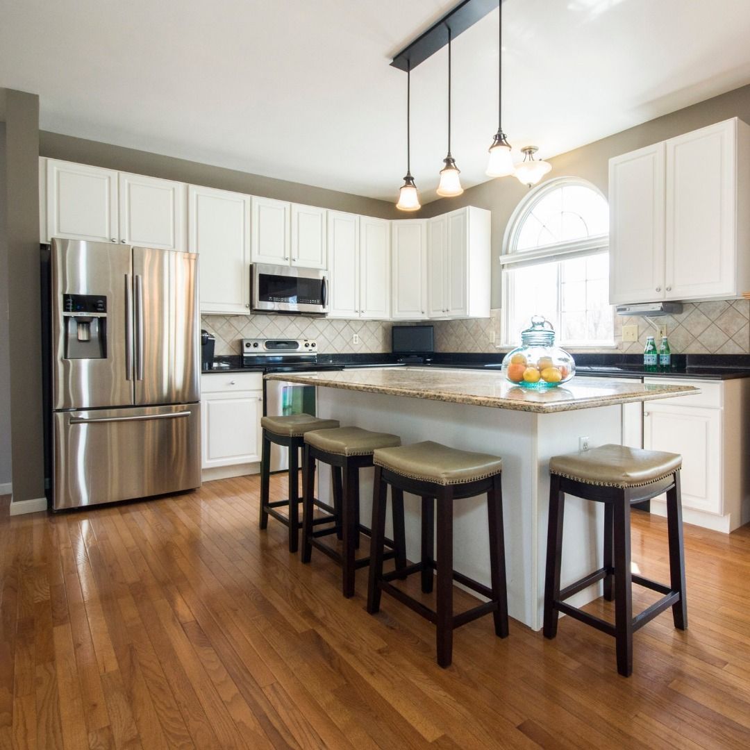 Spacious kitchen with white cabinets, stainless steel refrigerator, island with bar stools, and hardwood floors.