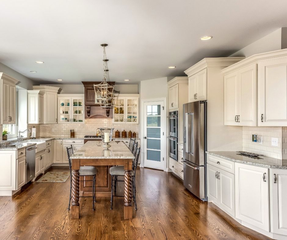 Spacious kitchen with wood floors, white cabinets, island, stainless steel appliances, and a light-filled space.