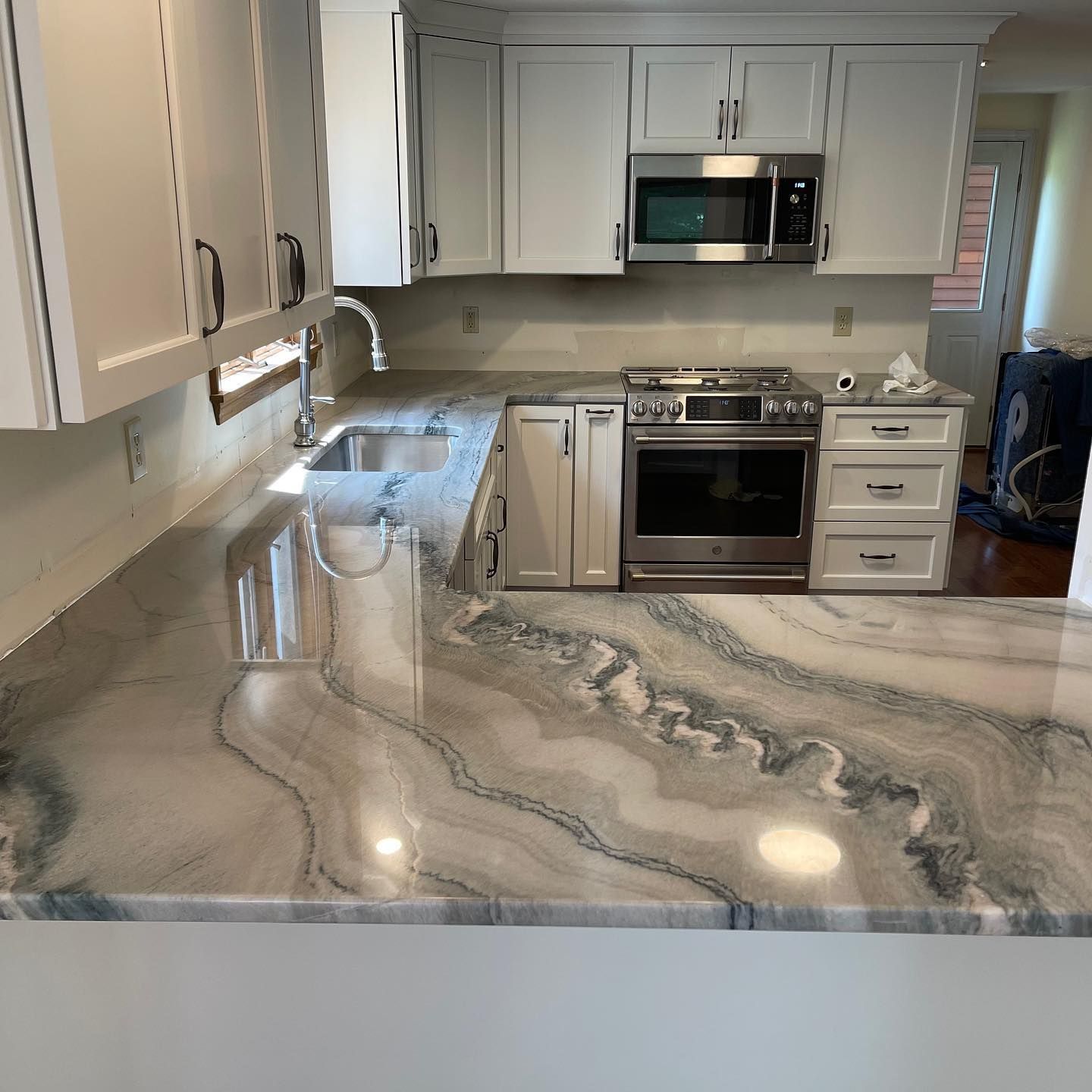 Kitchen with white cabinets, stainless steel appliances, and a countertop with swirling gray and blue patterns.