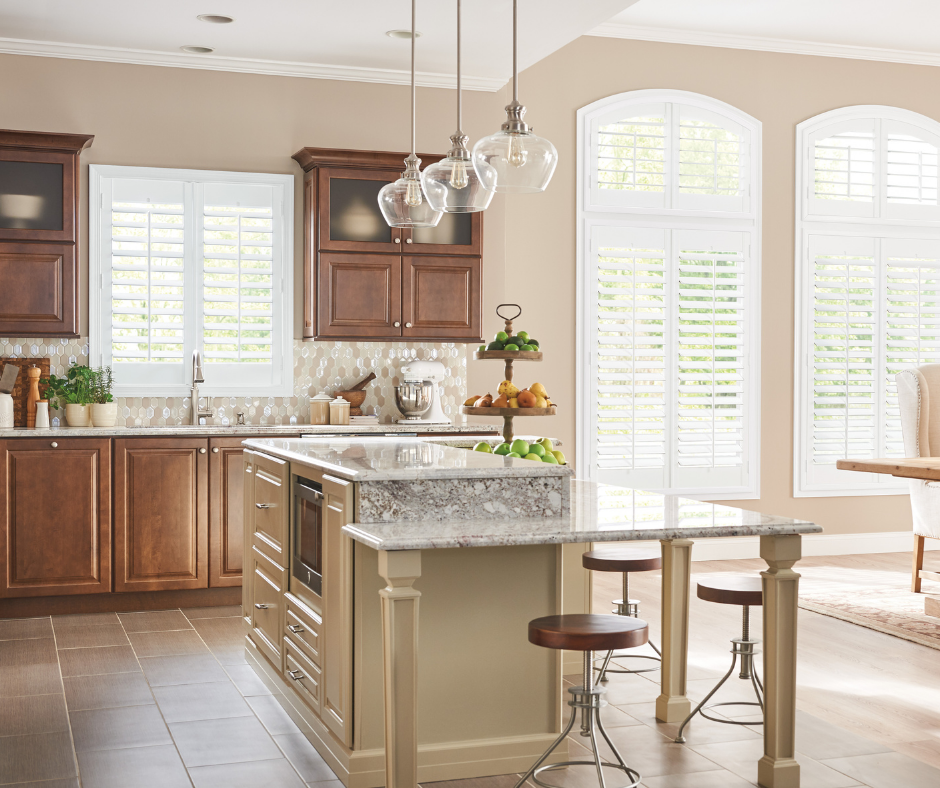 Kitchen with brown cabinets, island, arched windows with white shutters, and pendant lights.