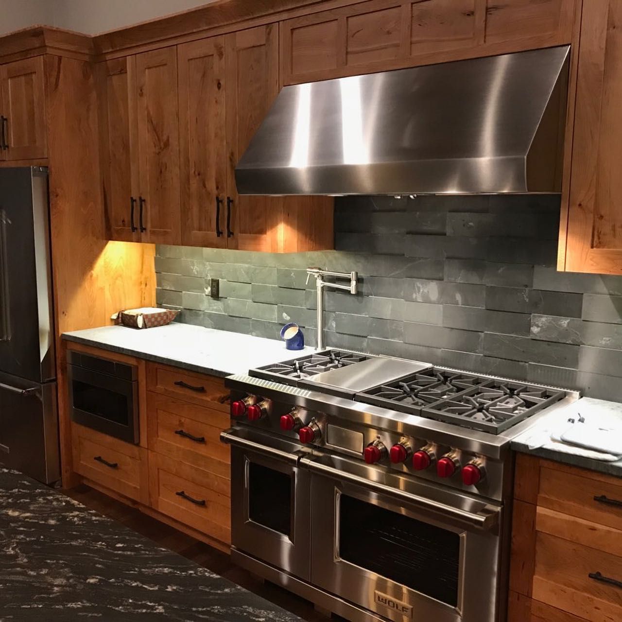 Kitchen with stainless steel appliances, light wood cabinets, and dark countertop, with a range and range hood.