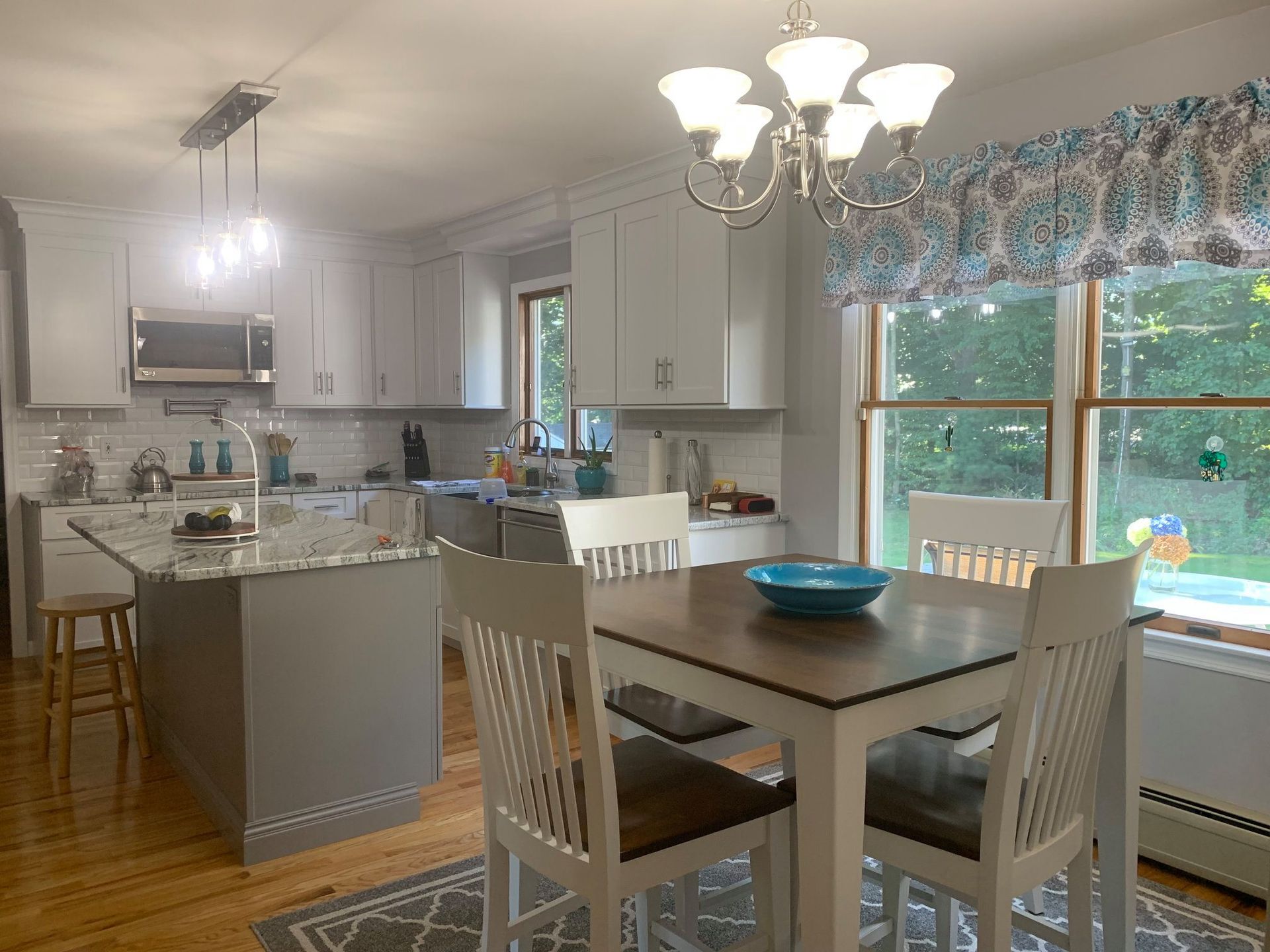 Kitchen with gray island, white cabinets, dining table with four chairs, and a window.