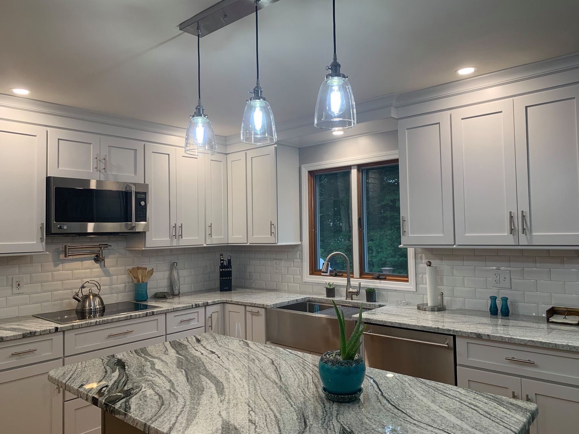 Bright white kitchen with granite island and pendant lights.