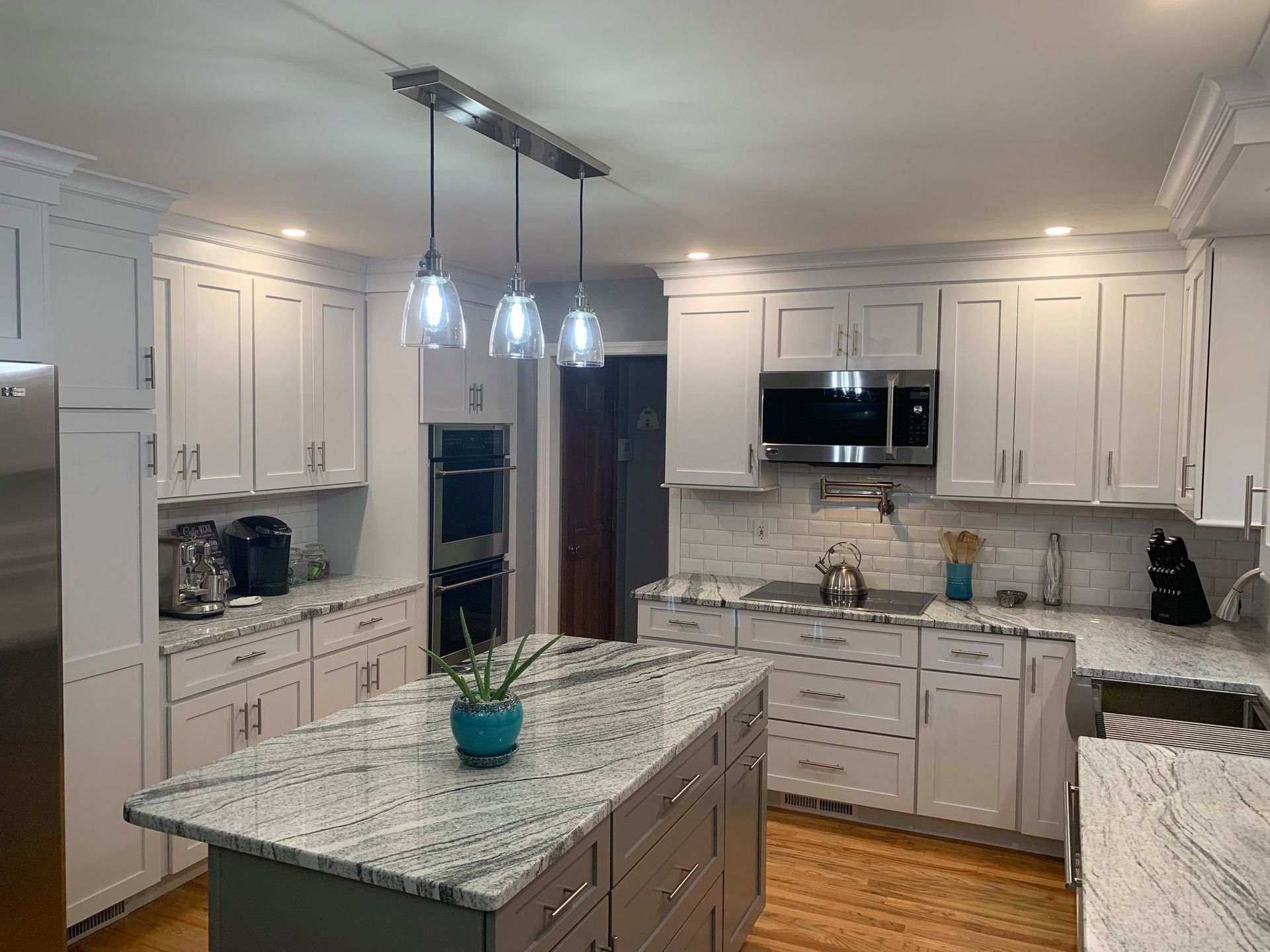 Bright white kitchen with light granite countertops and a central island. Pendant lights hang above the island.