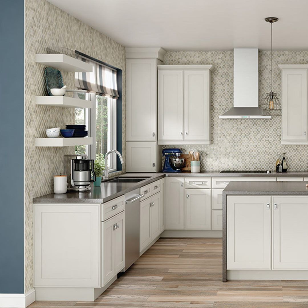 Modern white kitchen with stainless steel appliances, open shelving, and patterned backsplash.
