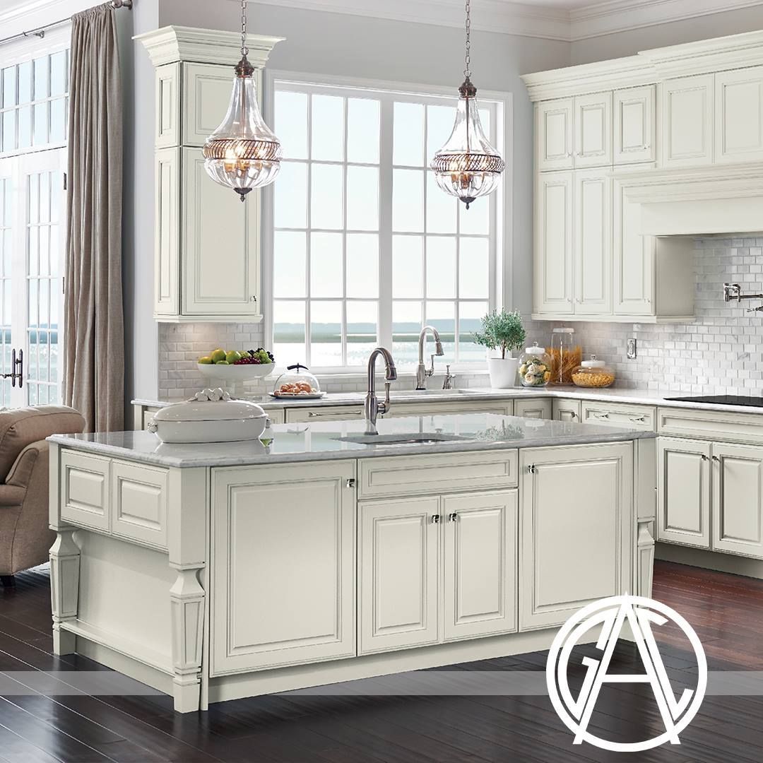 Cream-colored kitchen with island and ornate cabinets, two chandeliers, and large window.