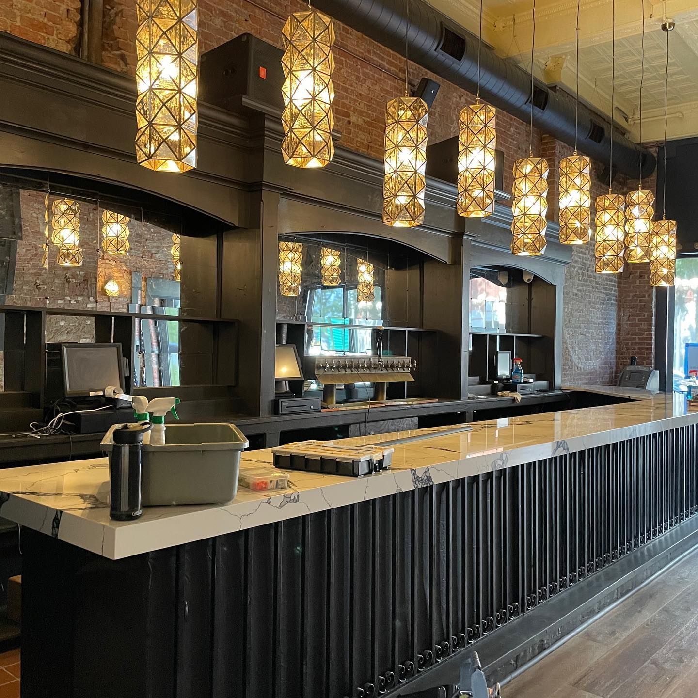 Empty bar with marble countertop, black trim, and decorative pendant lights. Brick wall in the background.