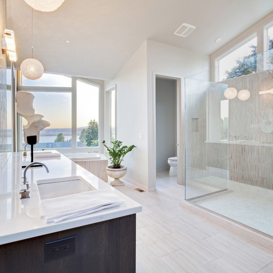 Spacious modern bathroom with white surfaces, large windows, glass shower, and view of water.