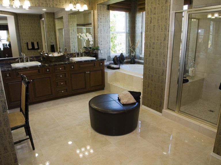 Luxurious bathroom with dark wood vanity, glass shower, soaking tub, and round ottoman.