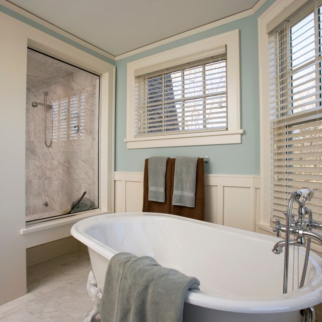 Bathroom with white clawfoot tub, shower, and window with blinds. Two brown towels hang on the wall.