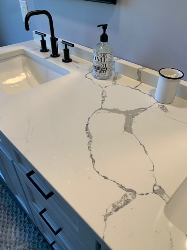 Bathroom vanity with white countertop, gray veining, black faucet, and accessories.