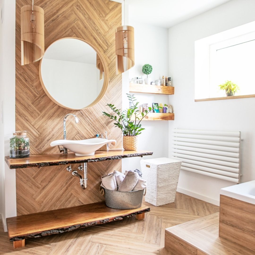 Bathroom with wooden accents. A round mirror hangs above a vessel sink. White walls and natural light.