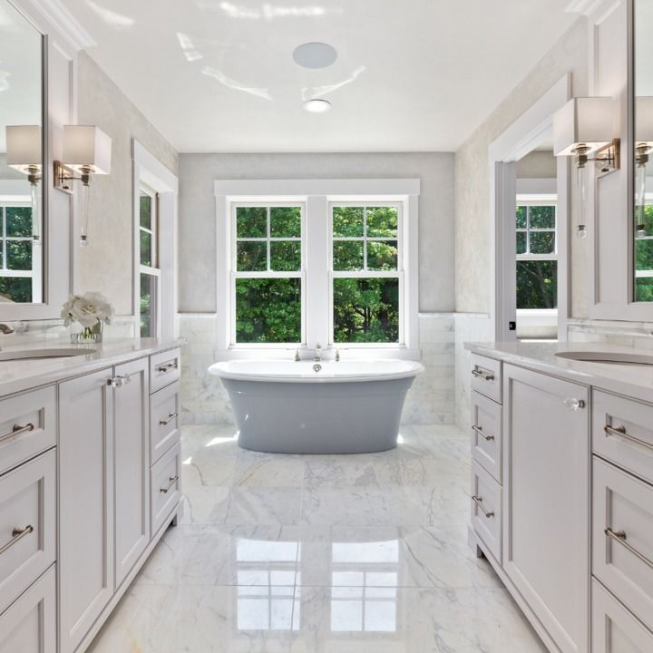 Bright white bathroom with marble floors, a freestanding gray bathtub, and a large window overlooking trees.