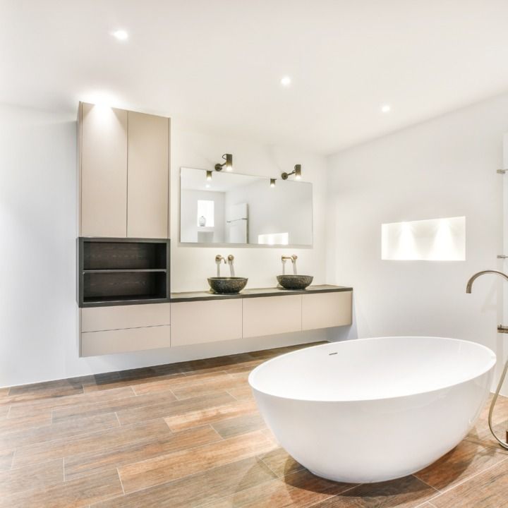 Modern bathroom with a white oval tub, floating vanity with two sinks, and wood-look tile floor.
