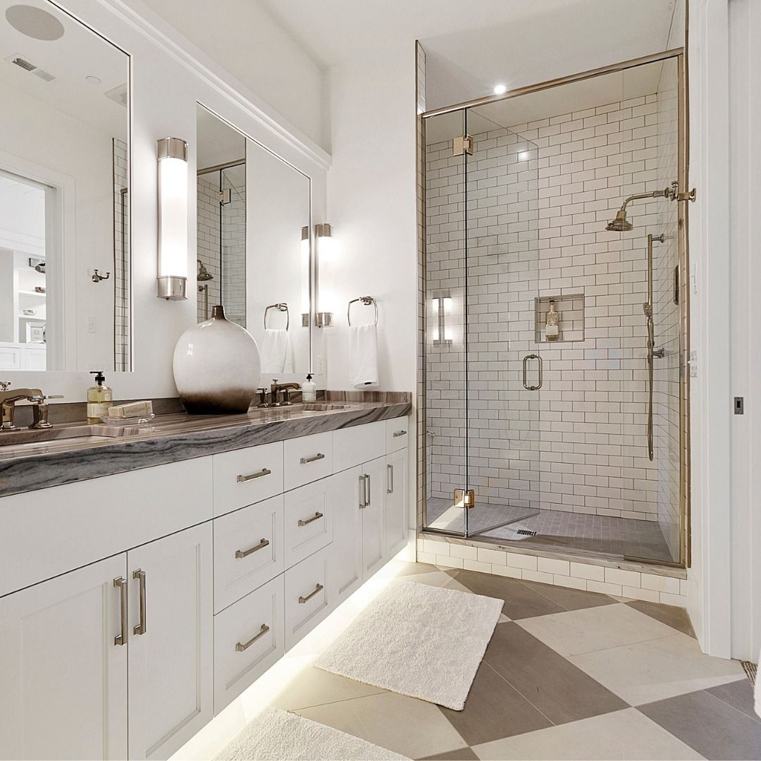 Luxurious white bathroom with double vanity, marble countertop, glass shower, and patterned floor.