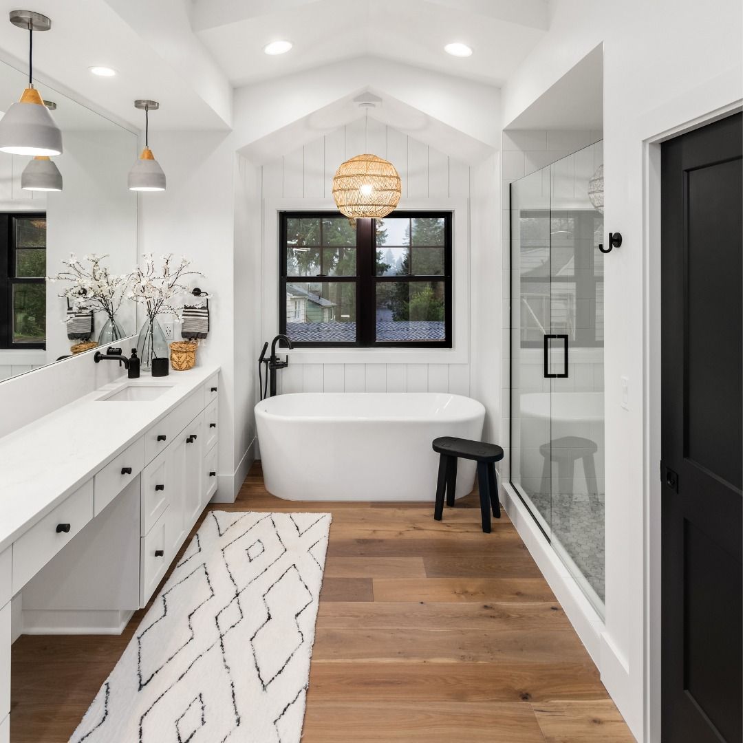 White modern bathroom with hardwood floor, soaking tub, glass shower, and black accents.