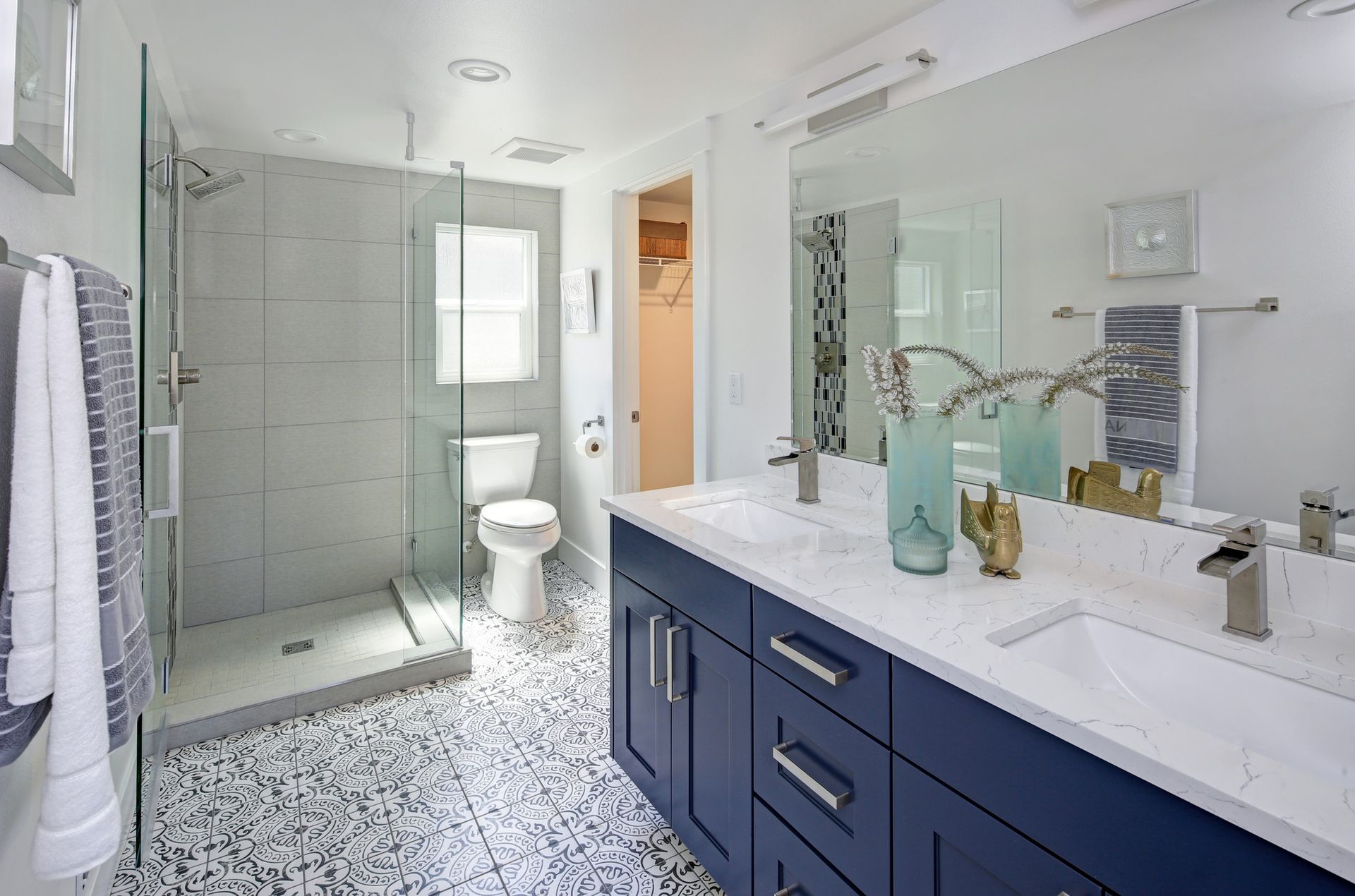 Modern bathroom with blue vanity, glass shower, pebble floor, and large mirror.