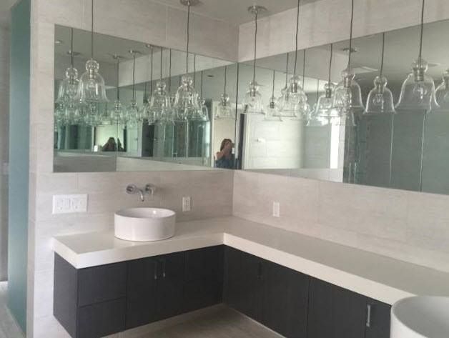 Modern bathroom with a large mirror, pendant lights, a white sink, and dark cabinets.
