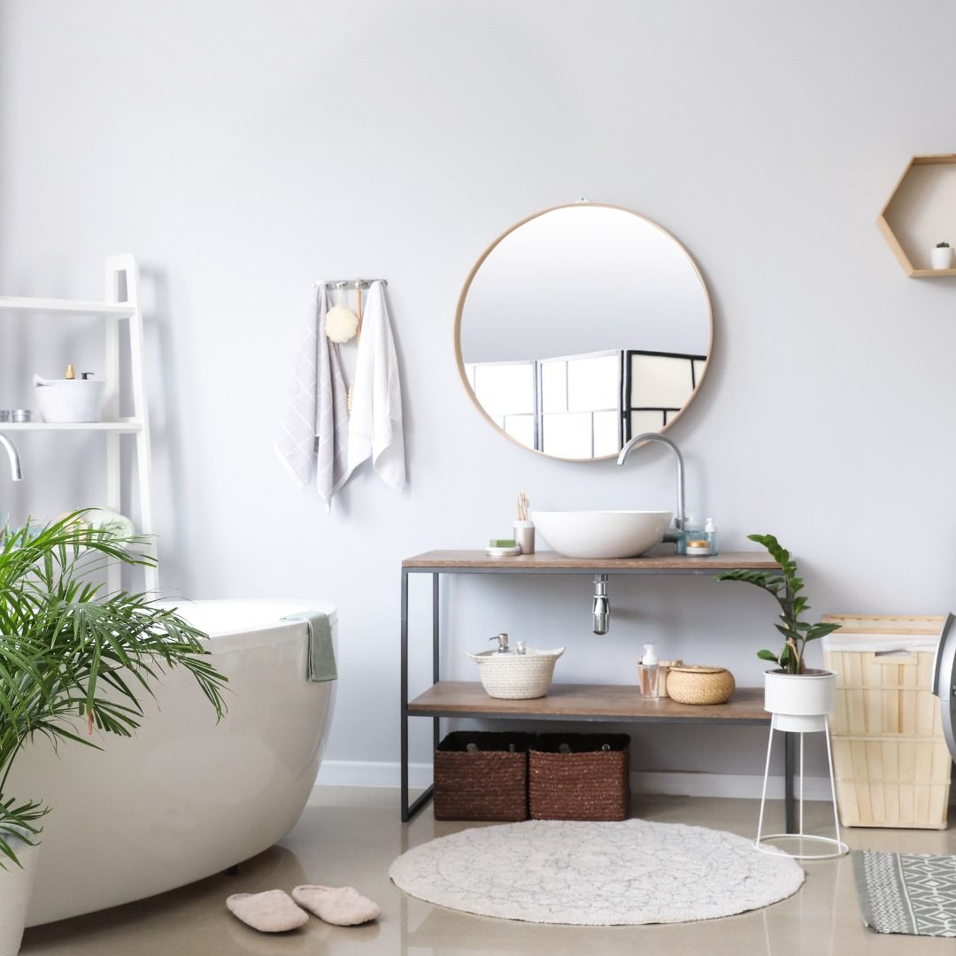 Bright bathroom with a freestanding tub, sink, mirror, and shelves. Neutral colors, plants, and natural light.