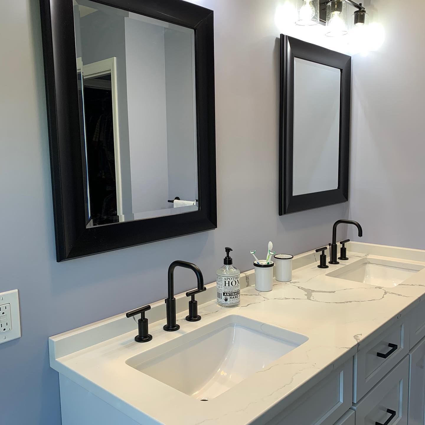Bathroom with two sinks, two mirrors, and black fixtures on a white countertop.