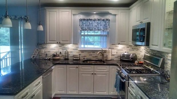 U-shaped kitchen with white cabinets, dark countertops, a window with floral valance, and stainless steel appliances.