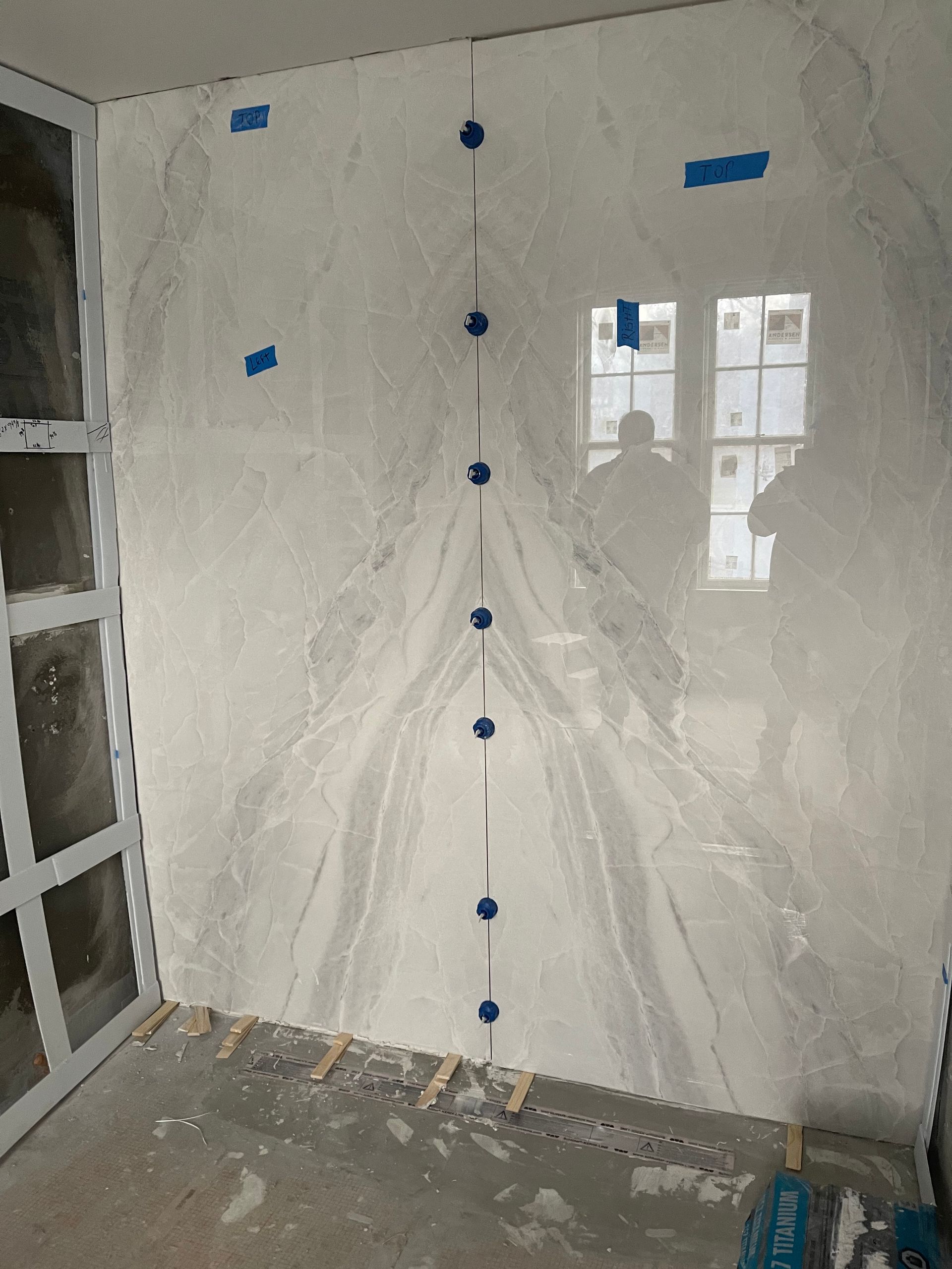 Large white marble slab installed on a wall. Blue tape and spacers used. Sunlight reflecting in window.