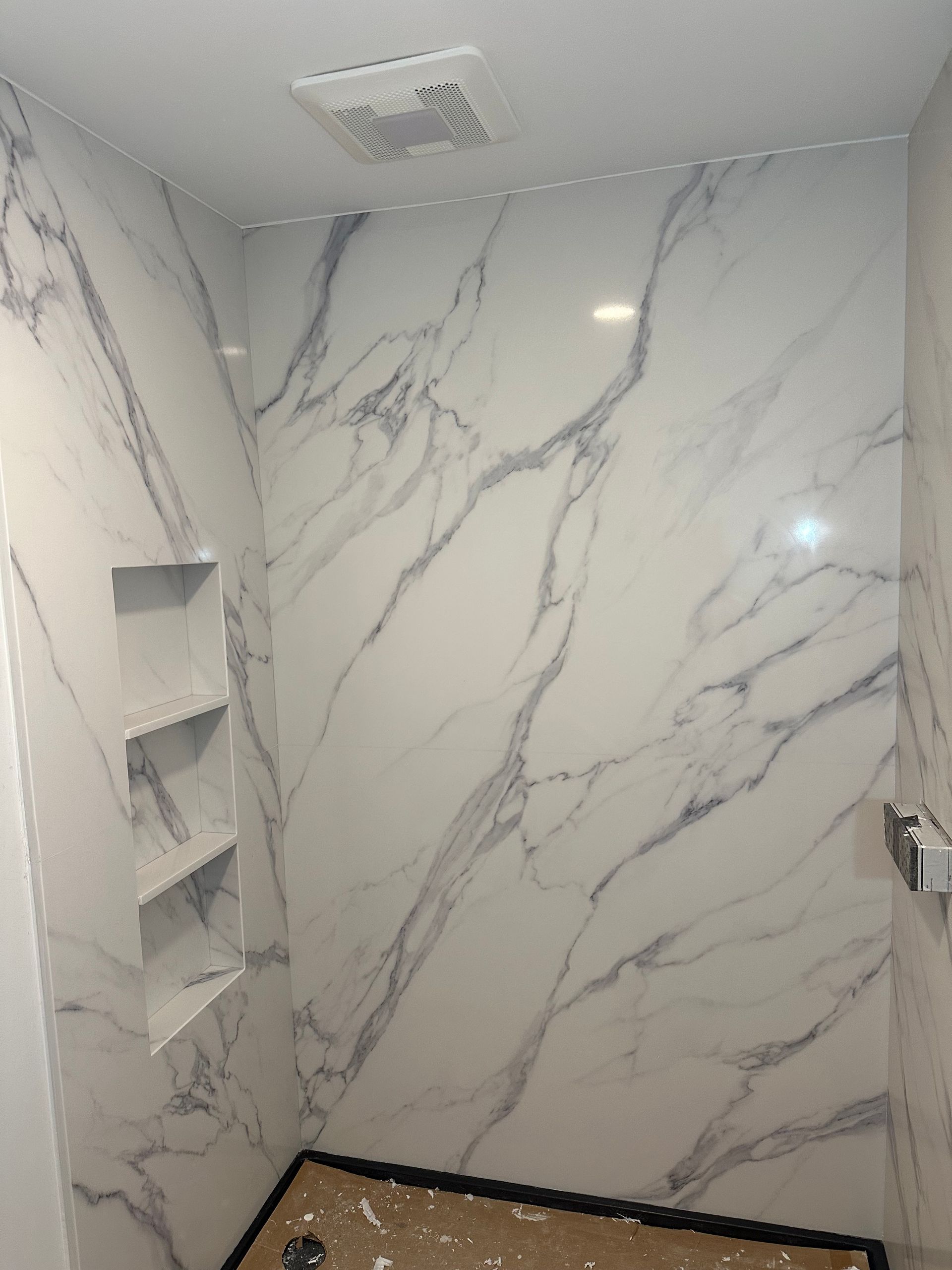 White marble-patterned shower walls with built-in shelves and a vent.