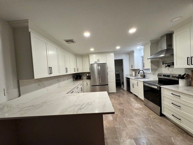 Modern white kitchen with stainless steel appliances, marble countertops, and dark handles.