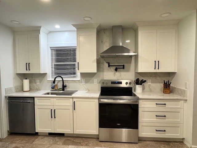 White kitchen with stainless steel appliances, cabinets, and a window.