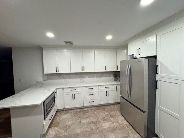 White kitchen with marble countertops, stainless steel refrigerator, and white cabinetry.