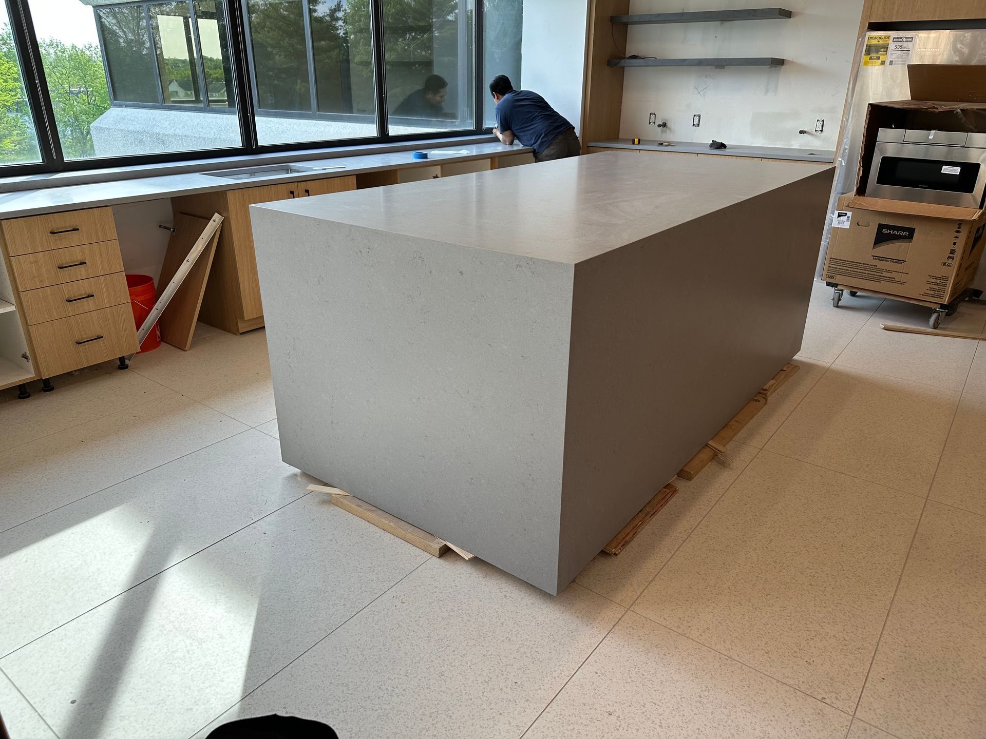 Large gray kitchen island in a room under construction, with a person working in the background.