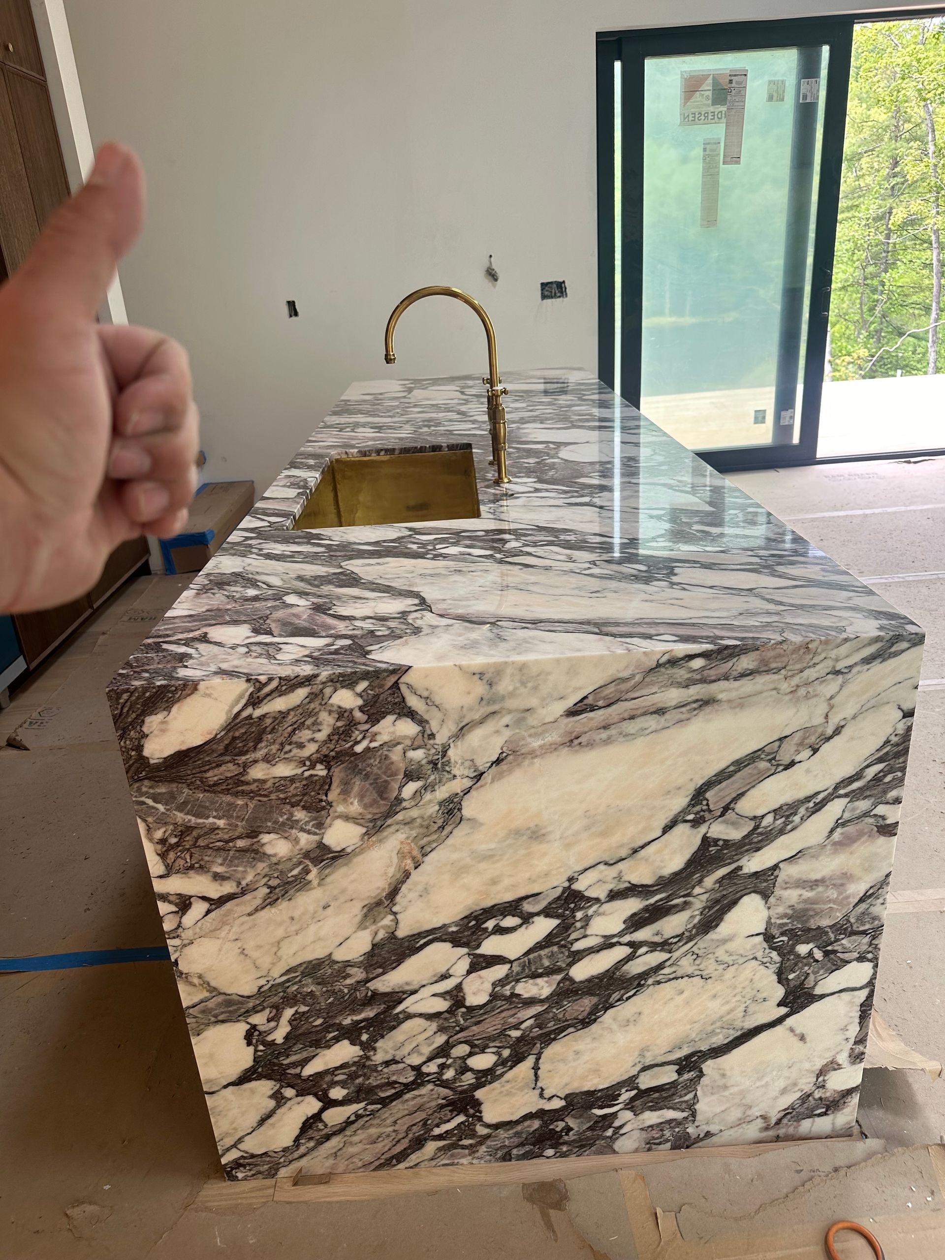 Kitchen island with white and purple marble, gold faucet and sink, hand giving a thumbs up.