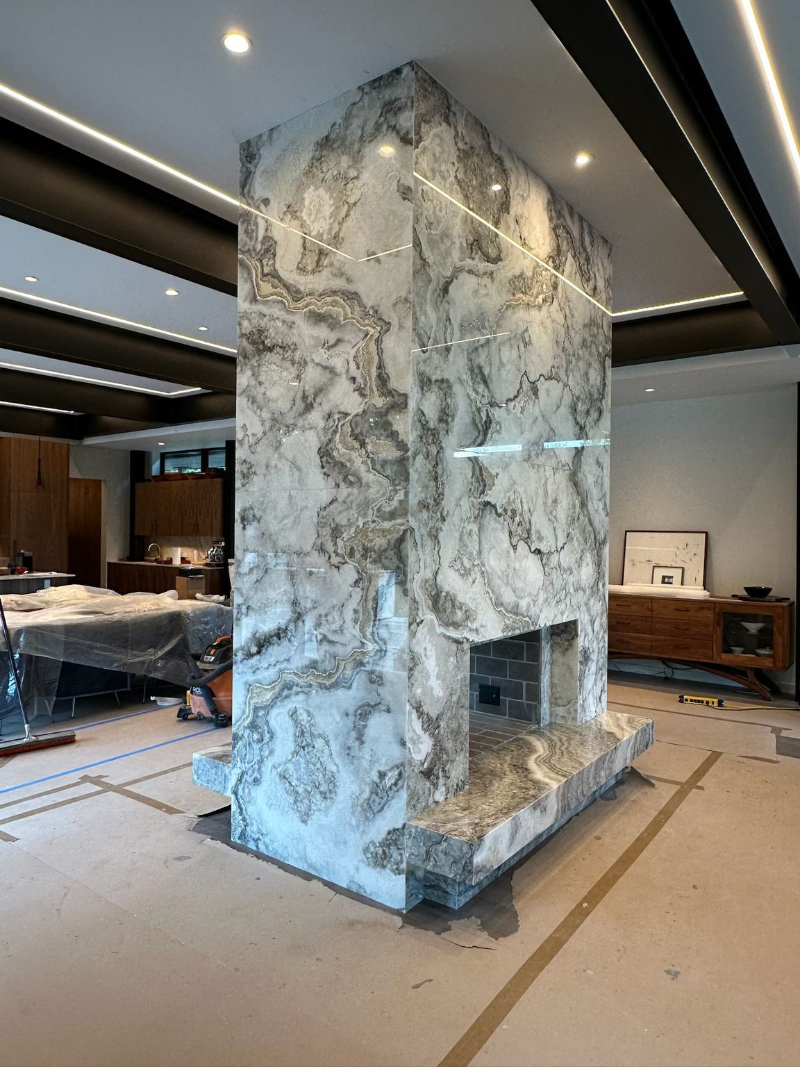Marble-clad fireplace in a modern interior, with gray and white veining, under construction.