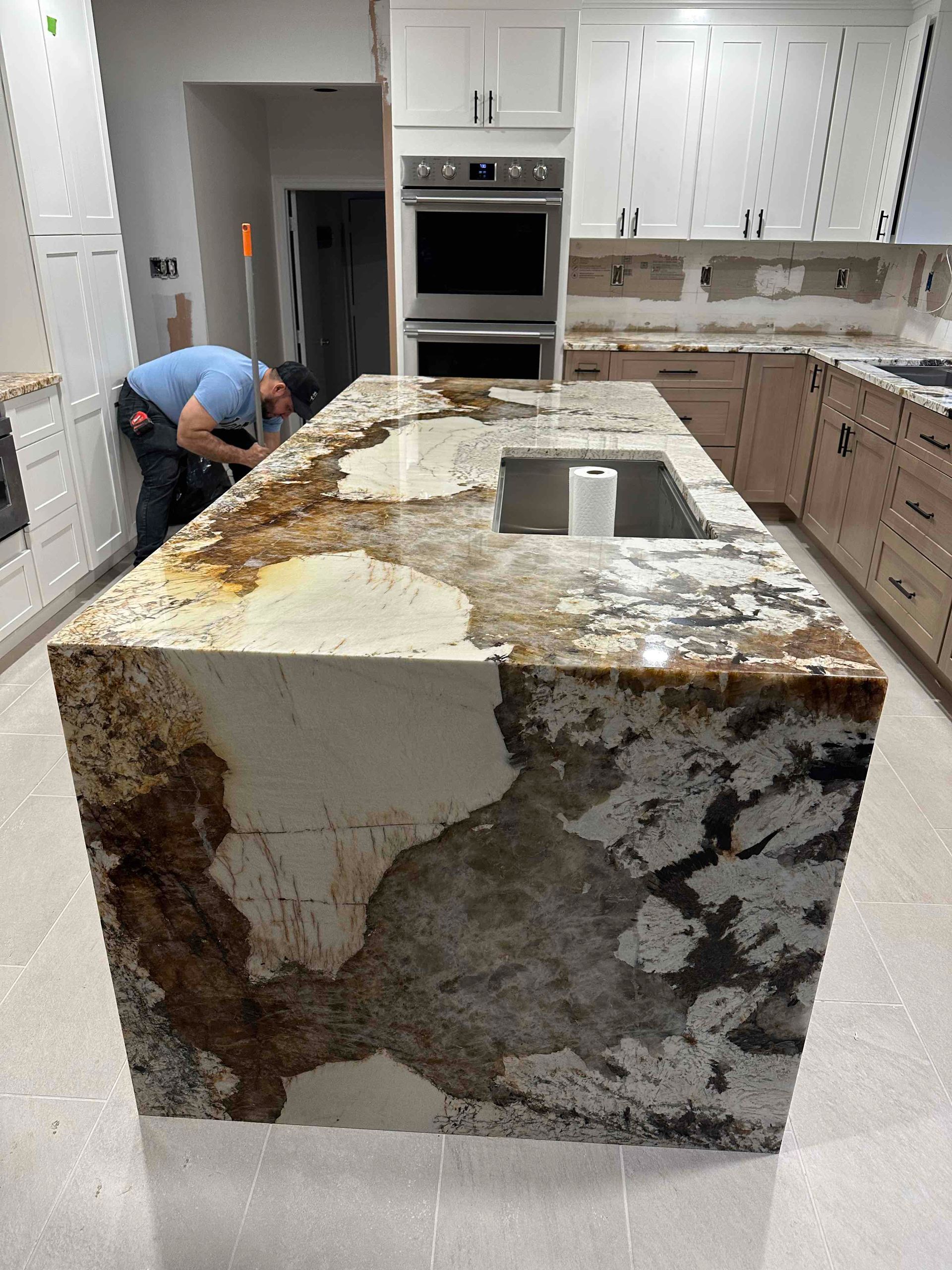 Kitchen with a large stone island countertop being installed, with a worker crouching on the left.