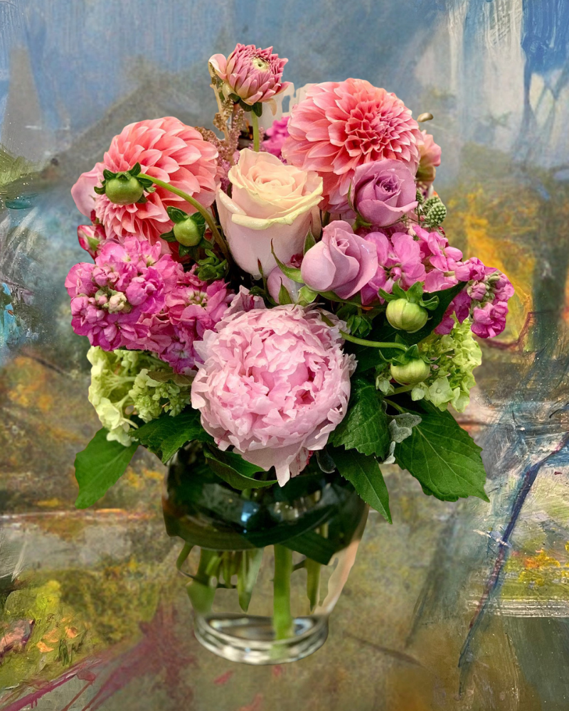 Pink and lavender flowers arranged in a glass vase against a painted backdrop
