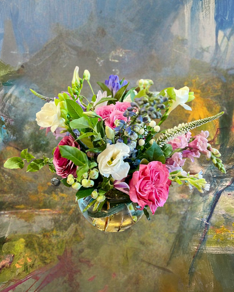 Colorful bouquet of pink, white, and yellow flowers in a glass vase against an abstract painted background