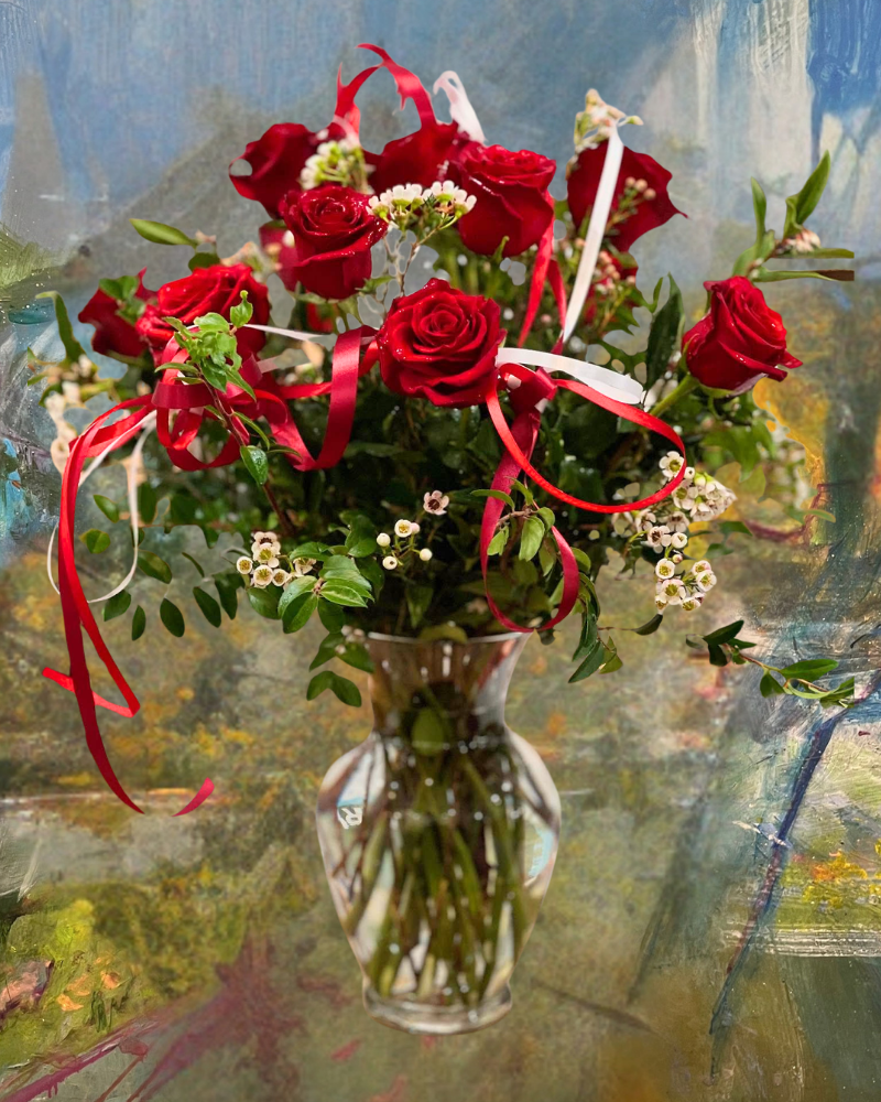 Red roses and white flowers in a glass vase with red ribbons, against an abstract painted background